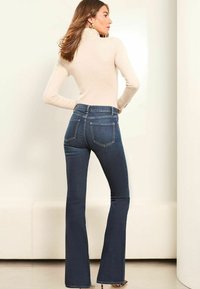 Hoge, uitlopende jeans in donkerblauwe denim, met een vijf-pocket ontwerp en een lichte stretch. Gecombineerd met een lichtbeige coltrui.