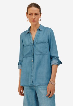 Hellblaues Denimhemd mit langen Ärmeln, knöpfbaren Manschetten, zwei Brusttaschen und einem Kragen. Endet hüftlang mit geradem Schnitt.