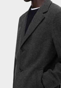 Blazer in misto lana grigio scuro con rever a punta, due bottoni e superficie testurizzata. Abbinate a un maglione scuro.