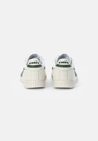 White and green low-top sneakers with a textured leather upper, featuring a ridged rubber sole and branded heel accents.