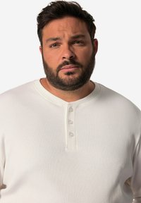 Weißes, geripptes Langarmshirt mit Henley-Ausschnitt und drei Knöpfen, weichem Stoff und entspannter Passform.