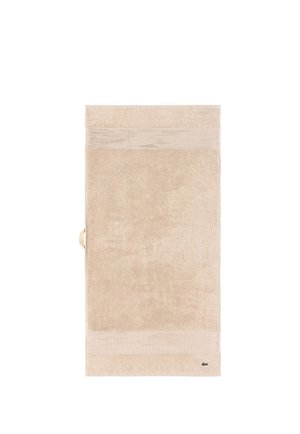 Serviette de bain rectangulaire beige avec des rayures horizontales texturées près des bords et un petit logo crocodile vert dans un coin.