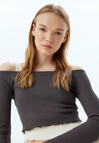 Geribbelde off-shoulder crop top in donkergrijs met contrasterende witte zoom. Lange mouwen, getailleerd ontwerp, textuurstof. Gladde afwerking, geen patronen.