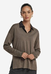 Brun stickad tröja med V-hals och längre bakstycke. Har en svart krage som tittar fram och ribbade mudd för extra struktur.