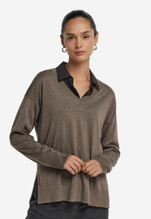 Brun strikket sweater med V-hals og længere bagkant. Har en sort krave, der stikker frem, og ribbede manchetter for ekstra tekstur.