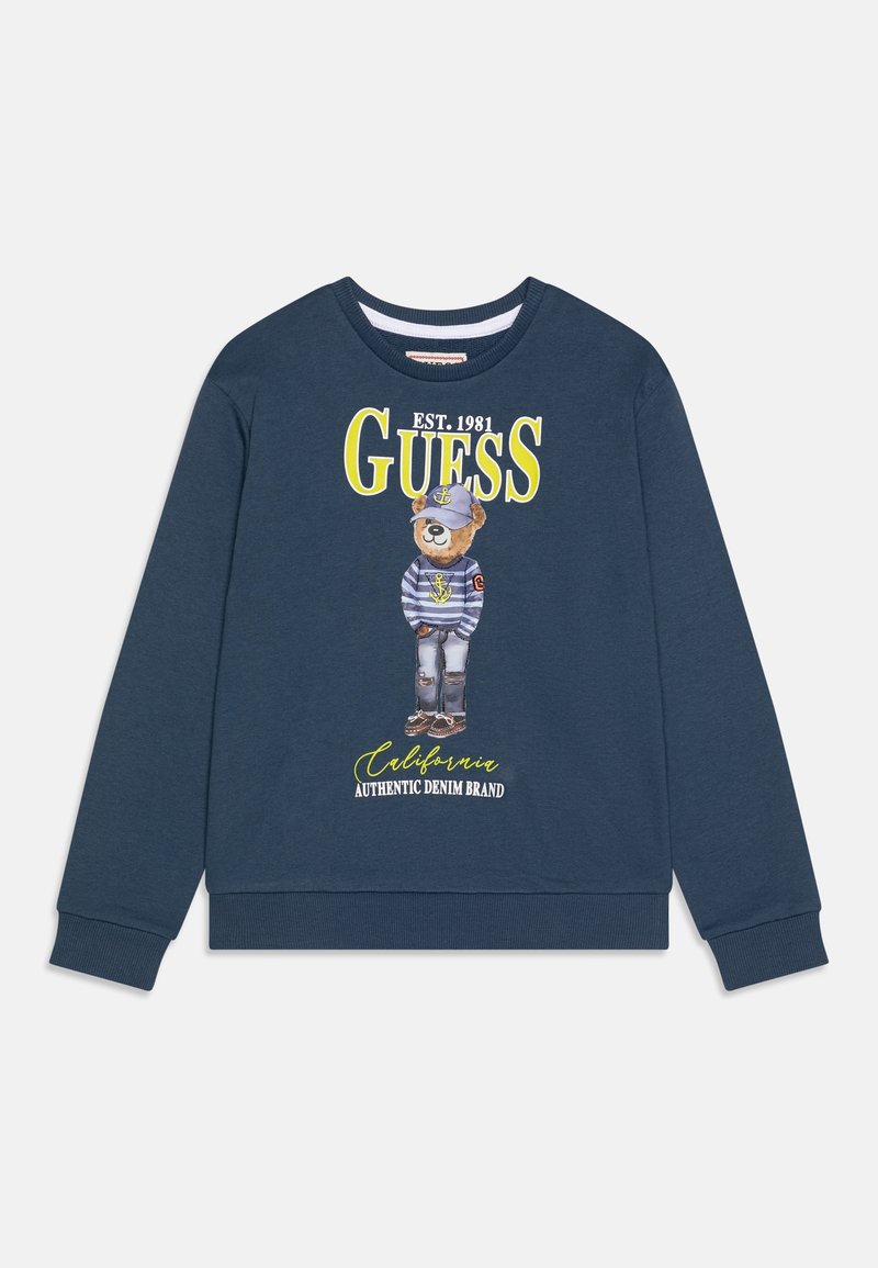 Granatowy sweter z niedźwiedziem w czapce marynarskiej i w paski koszulce, z napisem "GUESS EST. 1981 California Authentic Denim Brand" z przodu.