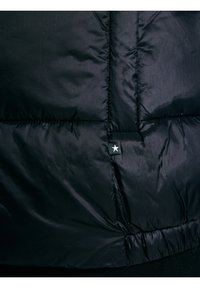 Mustast tikandist jopekangas lähedalt vaadatuna, mille keskmise õmbluse lähedal on valge tähega väike must silt.