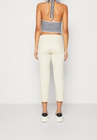 Beige, cropped broek met een aangesloten taille en een mid-rise ontwerp. De stof lijkt getextureerd, gecombineerd met een zwart-wit gestreepte cropped top en sneakers.