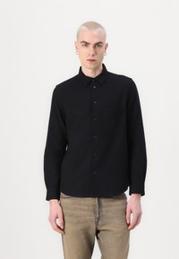 Black button-up shirt with a collar, single chest pocket, and long sleeves. Smooth texture. Worn with light-colored jeans.