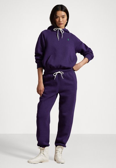 Purple sweatshirt with a hood and front pocket, paired with matching purple sweatpants. Features white drawstrings and a small green logo.