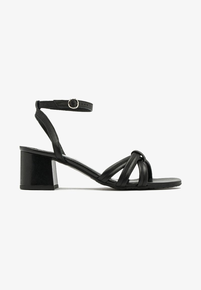 Sandale en cuir noir avec talon bloc, bride de cheville avec boucle et brides avant nouées sur fond blanc.