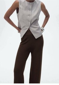 Débardeur à rayures gris clair sans manches avec cinq boutons et un design avant torsadé, associé à un pantalon évasé marron en tissu texturé.