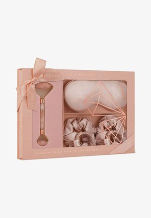 Jadeitowy rolka do twarzy, jedwabna maska na oczy i scrunchies zapakowane w jasnoróżowe pudełko z wstążką, ozdobione geometrycznymi akcentami w kolorze różowego złota.