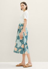 Un haut de couleur claire associé à une jupe mi-longue avec un fond turquoise et des motifs floraux abstraits en pêche et bleu clair.