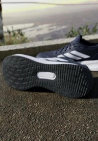 Black sports shoe featuring a textured rubber sole, white accents, and a smooth synthetic upper. Angled view shows detailing and tread pattern.