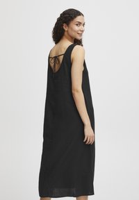 Rochie neagră din in, cu o croială lejeră, având bretele subțiri și spate cu decupaj în formă de cheie legat cu o fundiță. Textură fină și design până la gleznă.