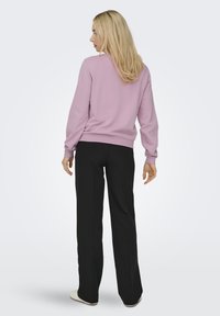 Lichtroze sweatshirt met lange mouwen, ribgebreide boorden en zoom, gedragen met zwarte broek. Gladde textuur, minimalistisch ontwerp, casual pasvorm.