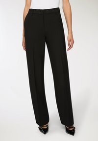 Czarne eleganckie spodnie o wysokim stanie, charakteryzujące się gładką teksturą i dopasowanym krojem. W zestawieniu z wskazówkowymi lakierkami.
