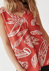 Top rosso senza maniche con design a foglia bianca, realizzato in tessuto morbido, con scollatura a V e vestibilità rilassata.