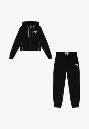 Felpa nera corta con zip e dettagli bianchi, con logo, abbinata a pantaloni della tuta neri coordinati con vita a coulisse e dettaglio logo.