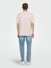 Light pink cotton t-shirt with a crew neckline, paired with light blue denim jeans. Model shown from the back, wearing white sneakers.