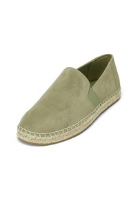 Chausson vert en daim avec panneaux latéraux élastiques, semelle intermédiaire en jute tissé et tige lisse, mettant en avant un design minimaliste.