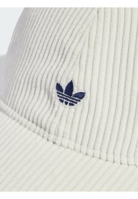 Fehér kordbársony női kalap, amely texturált felülettel rendelkezik, és az oldalán egy kék hímzett Adidas háromlevelű logó található.