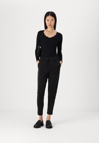 Haut noir à manches longues avec un col festonné, associé à un pantalon de jogging noir pailleté et des chaussures noires à enfiler.