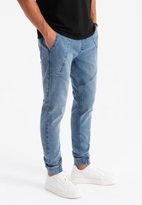 Pantalones jogger de color azul claro con un acabado de denim texturizado, que cuentan con bolsillos laterales y un corte ajustado, combinados con zapatillas blancas.