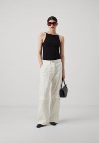 Top nero senza maniche, pantaloni cargo bianchi a gamba larga con tasche, borsa nera e occhiali da sole scuri. Tessuto morbido, vestibilità comoda.