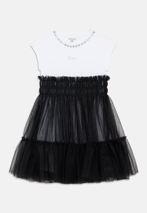 White short-sleeve top with rhinestone necklace detail and "Guess" logo paired with a black ruched tulle skirt with ruffled hem.