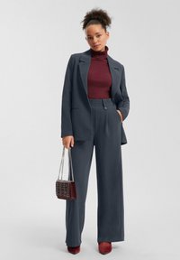 Completo grigio con blazer su misura e pantaloni a vita alta. Collo alto color bordeaux sotto, borsa bordeaux e tacchi abbinati.