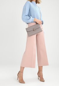 Svetle modrý žebrovaný svetr, růžové široké cropped kalhoty, šedá taška přes rameno a nahé sandály na kotníku vytvářejí moderní, koordinovaný vzhled.