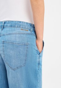 Hellblaue Jeans aus Denim, mit einer Gesäßtasche, genähten Details und einem Logo am Bund. Glatte Textur, normale Passform.
