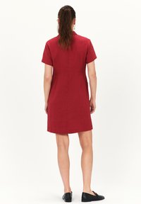Kurzes rotes Kleid, A-Linie Design, knielang, aus strukturiertem Stoff, mit einer Rückennähten-Details, getragen mit schwarzen flachen Schuhen.