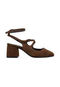 Zapatos de ante marrón con tacón cuadrado y punta afilada, que presentan una correa en el tobillo y un diseño recortado, acabado texturizado y detalle de hebilla ajustable.