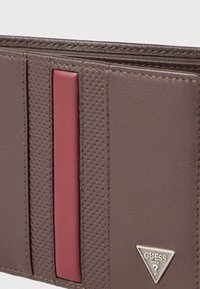 Bruine leren portemonnee met een rode accentstreep, met een getextureerd oppervlak, gestikte randen en een klein logo in de onderste hoek.