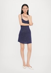 Abito senza maniche di un blu navy, realizzato in tessuto scintillante; silhouette attillata con scollo rotondo e orlo svasato. Texture liscia e design minimale.