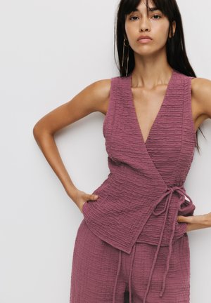 Wrap top in textured, mauve fabric with a deep V-neck and tie detail at the waist, paired with matching loose bottoms.