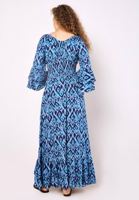 Maxikleid mit gerafftem Rücken. Blaues und türkisfarbenes geometrisches Muster. Lange, weit geschnittene Ärmel und Volant-Saumdetails. Leichter Stoff.