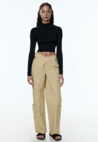 Zwarte geribbelde lange mouw crop top, gecombineerd met beige wijde cargo broek met zij uitsnijdingen en borstzakken.