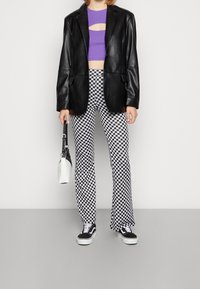 Svart läderblazer, lila kort topp med utskärning, rutiga utsvängda byxor, svartvita sneakers och en liten vit handväska.