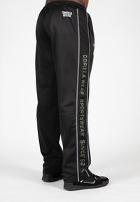 Zwarte sportbroeken met een mesh-textuur, contrasterende groene en witte strepen, en het merklogo "GORILLA WEAR" prominent weergegeven.