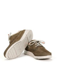 Zapatos de ante marrón con suelas blancas, que presentan un diseño perforado, costuras en contraste y cordones grises. Los acentos incluyen un pequeño detalle en naranja.