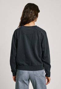 Sudadera negra con textura acanalada, cuello redondo y mangas largas; combinada con unos vaqueros de cintura alta en gris claro que cuentan con bolsillos traseros.