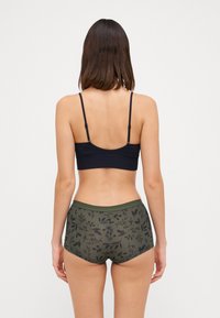 Čierny bralet s tenkými ramienkami v kombinácii s vysokými zelenými nohavičkami so kvetinovým vzorom. Hladká textúra, jednoduchý dizajn, žiadne viditeľné kovanie.