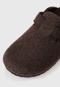 Brown felt slipper with a rounded toe, soft texture, and a plain design. Features a strap across the top and a black rubber sole.
