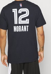 Černý basketbalový dres s odvážným bílým textem "12" a "MORANT" na zádech. Vyrobeno z prodyšného síťovaného materiálu.