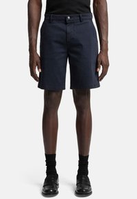 Shorts en tissu bleu marine avec un devant plat, des passants de ceinture et une fermeture à un bouton. Caractérisés par une coupe ajustée et des poches latérales.