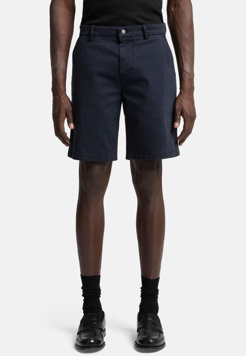 Shorts en tissu bleu marine avec un devant plat, des passants de ceinture et une fermeture à un bouton. Caractérisés par une coupe ajustée et des poches latérales.